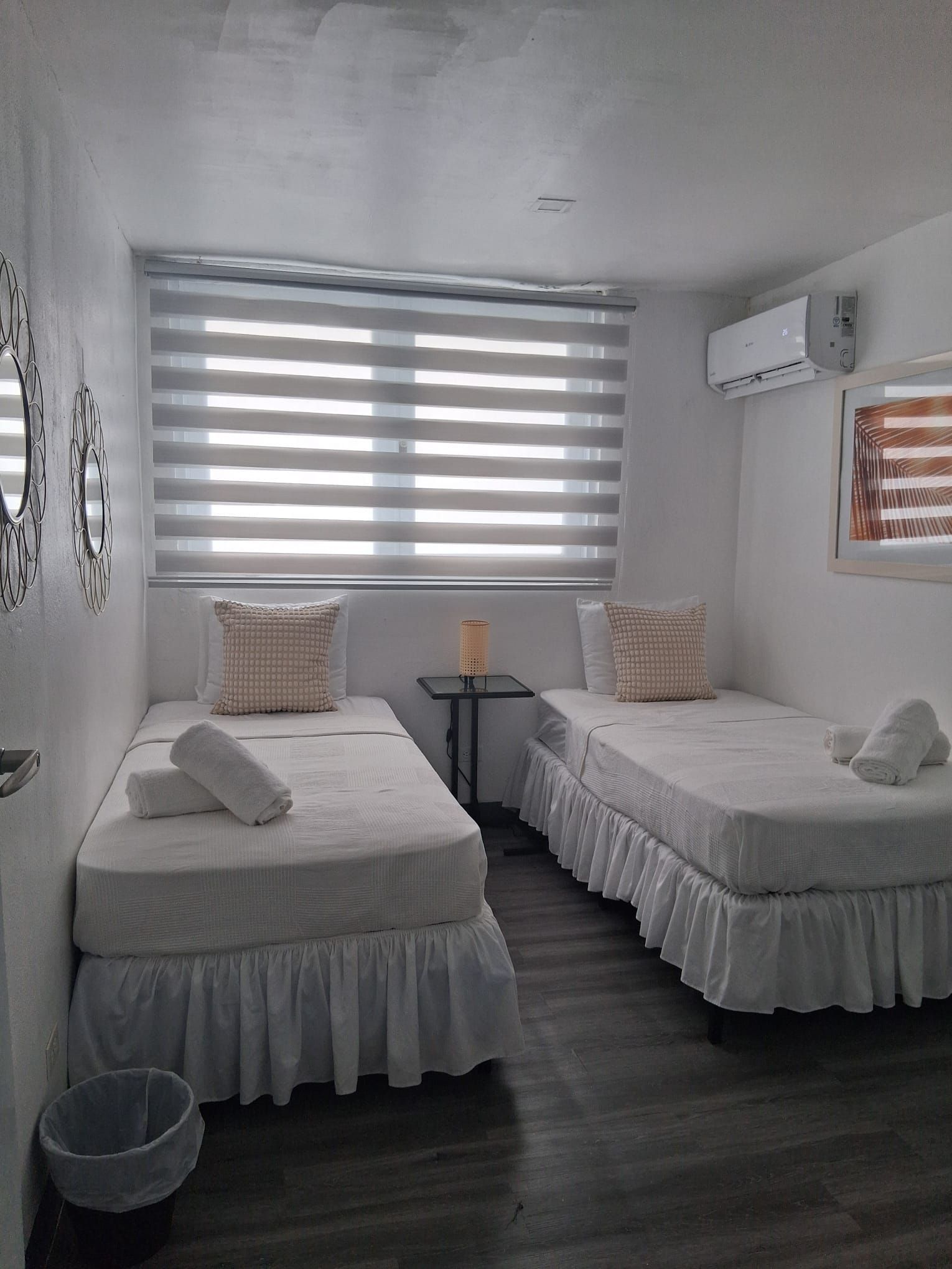A room with two beds, a small table, and a trash bin.