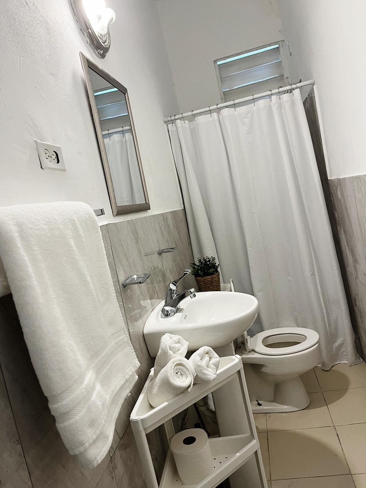 A bathroom with a sink, toilet, and a mirror. There is a towel rack with towels and a small shelf with toiletries.