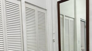 A room with white louvered closets, a large mirror, and a vase with dried flowers. - Janer House (San Juan)
