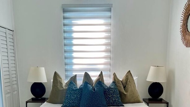 A bedroom with a bed, two bedside tables, a window with blinds, and a wall-mounted air conditioner. - Janer House (San Juan)