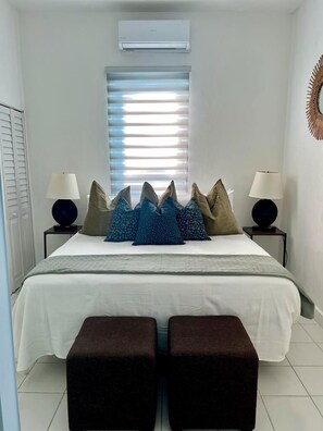 A bedroom with a bed, two bedside tables, a window with blinds, and a wall-mounted air conditioner. - Janer House (San Juan)
