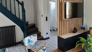 Un escalier avec des balustrades sombres, un sol à motifs, un mur lambrissé en bois orné d’un téléviseur à écran plat, et un fauteuil à motifs floraux.