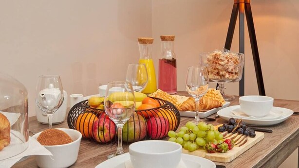 En frukostbuffé med olika sorters frukt, bakverk och drycker, uppdukad på ett träbord.