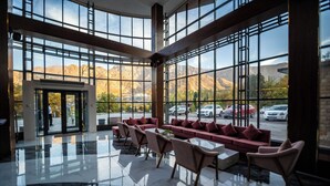 Un vestíbulo amplio con un diseño moderno, que incluye una zona de estar con sofás y sillones, ventanas grandes con vistas a la montaña y un suelo reflectante.