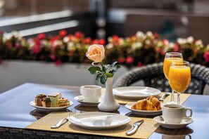 A breakfast table with pastries, a vase with a single rose, and two glasses of orange juice.