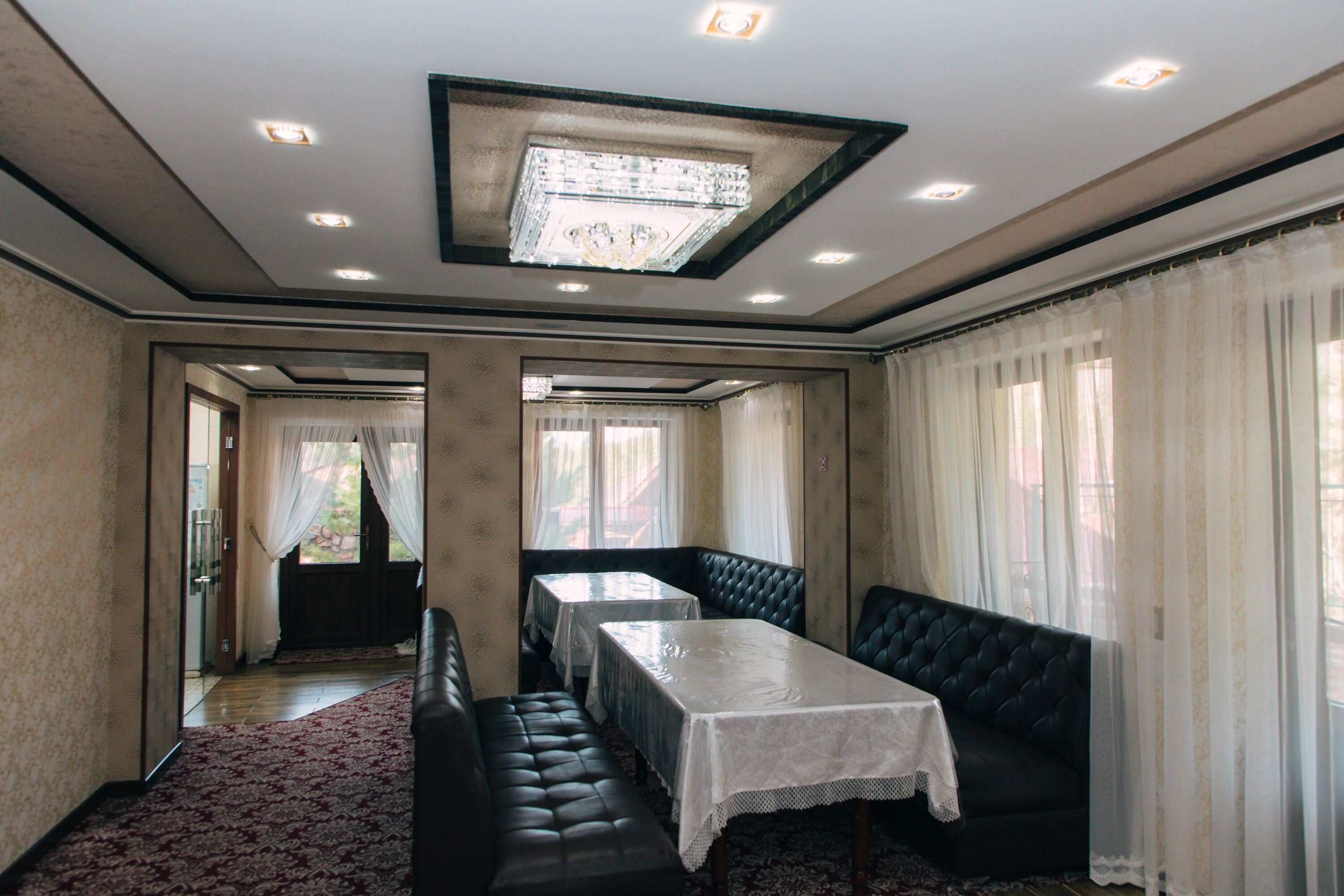 Una habitación con una mesa grande, un sofá y un banco. Hay cortinas en las ventanas y un candelabro en el techo.