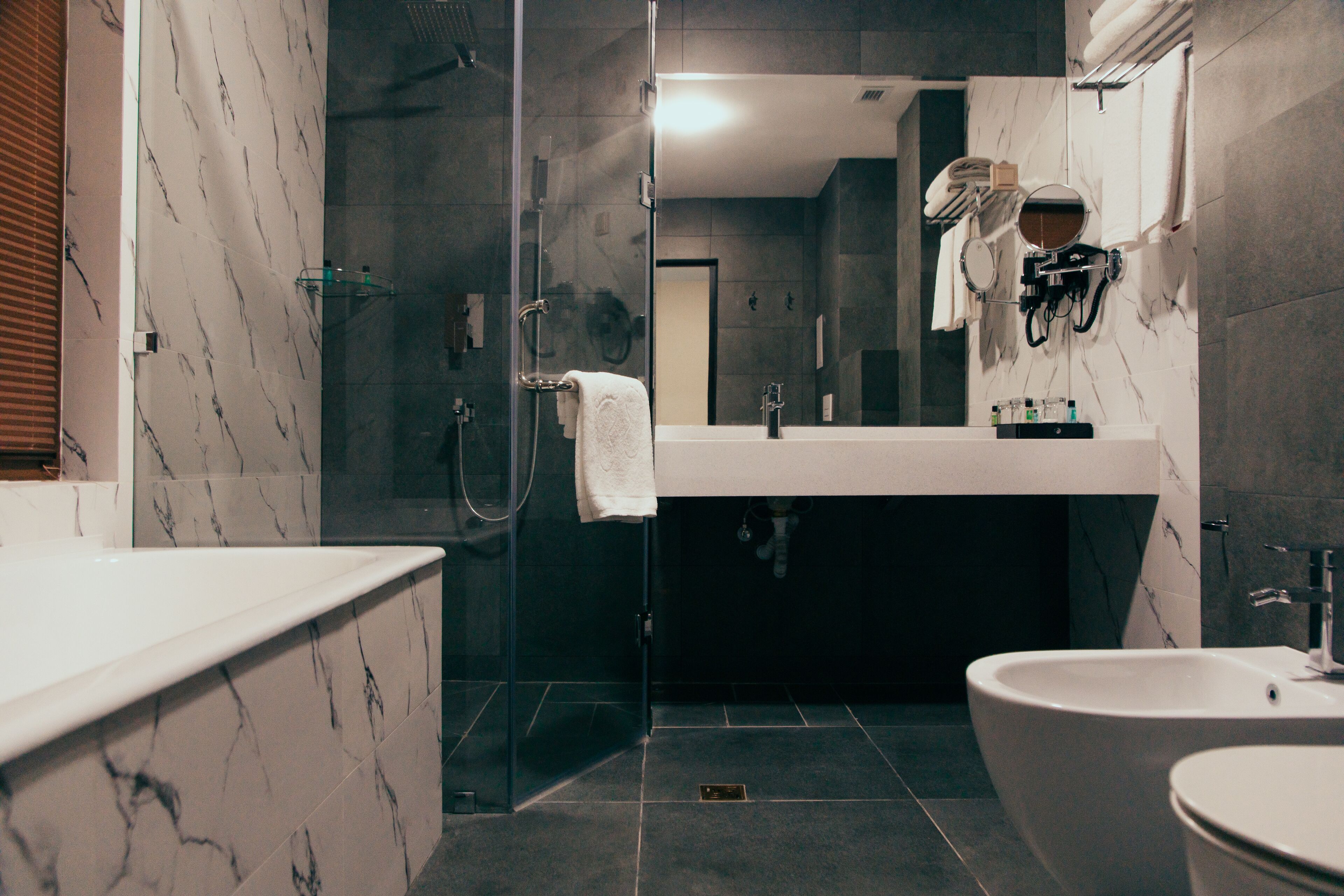 Ein modernes Badezimmer mit einer Glaskabine zur Dusche, einer freistehenden Badewanne und einem Waschtisch mit Spiegel.