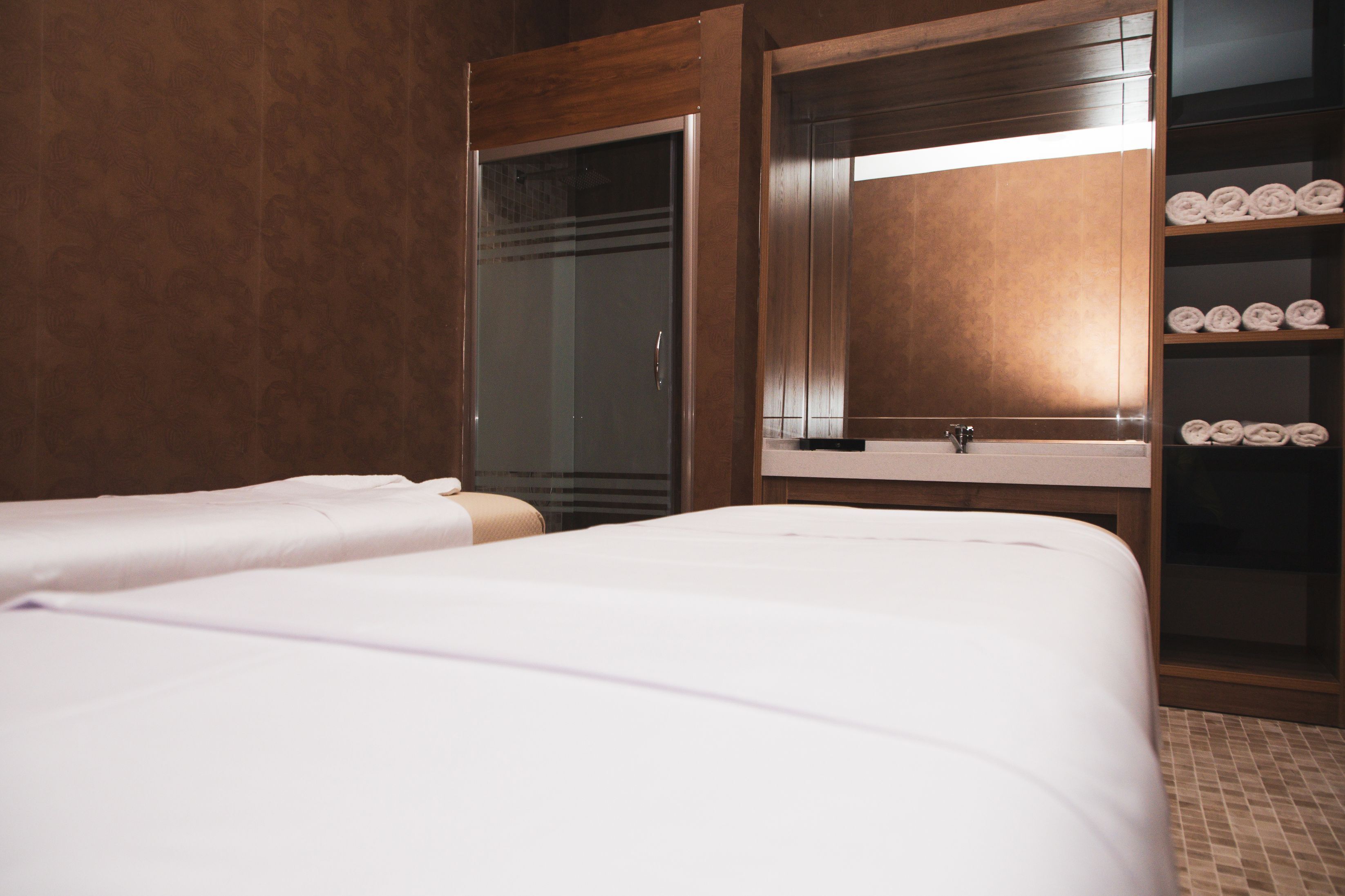 Habitación de hotel con dos camas, un espejo grande, un armario de madera y un estante con toallas.