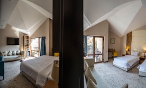 A spacious hotel room with a large bed, a sofa, a TV, and a balcony with a view.