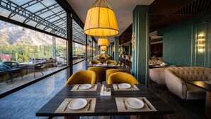 Un restaurante con mesas dispuestas para comer, un sofá y vistas a montañas a través de grandes ventanales.