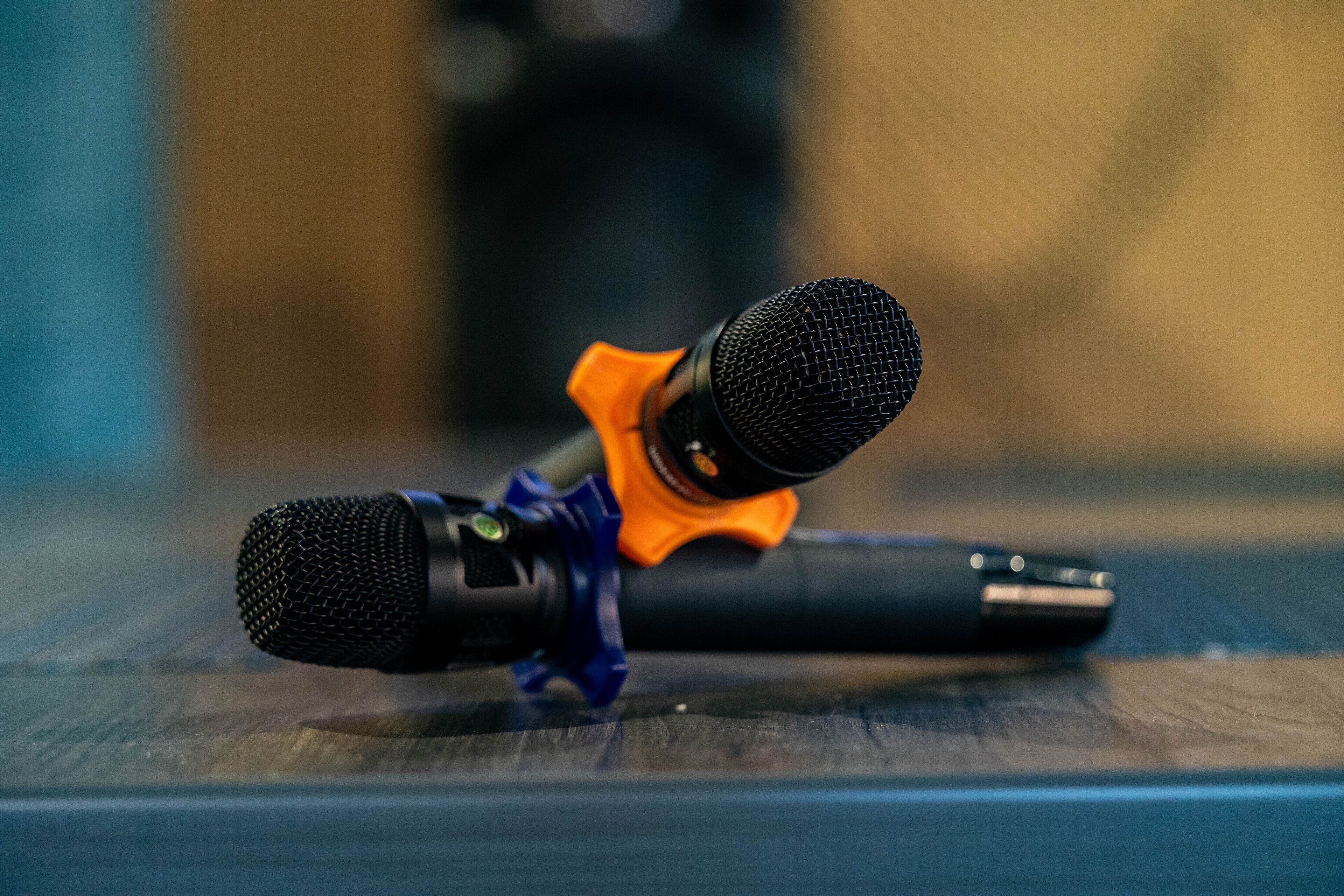 A microphone with an orange and blue stand on a wooden surface.