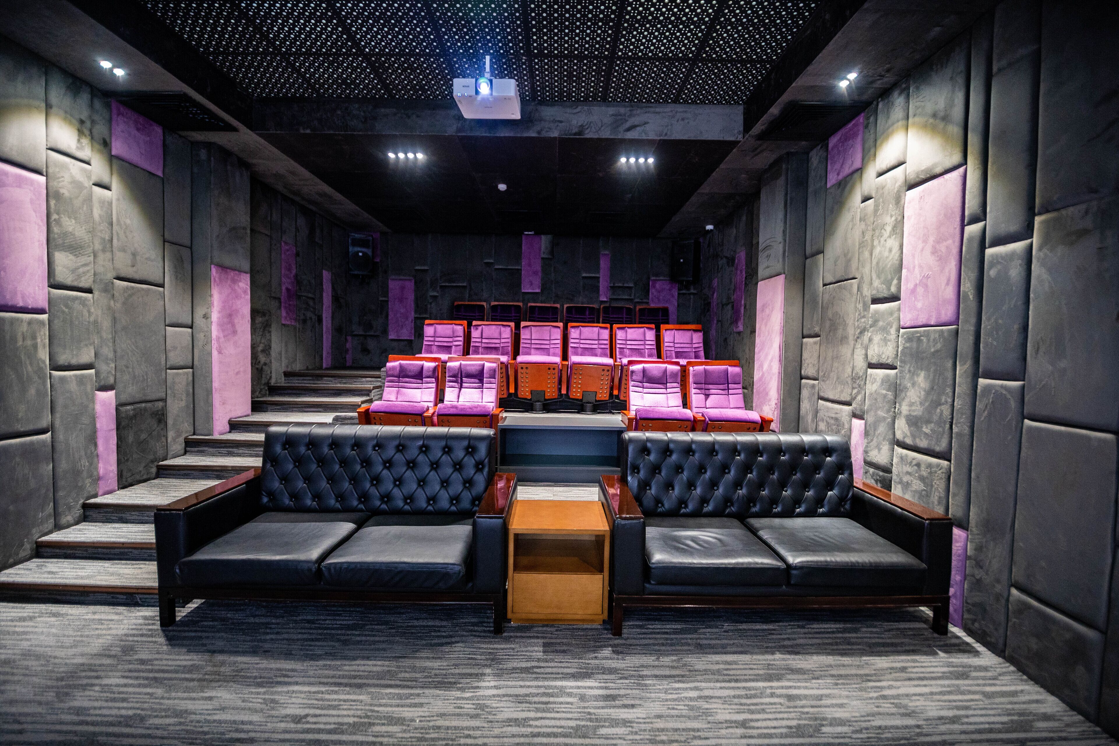 A theater with tiered seating, plush black and purple upholstered seats, and a central stage area.