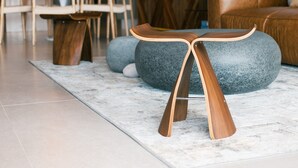 Een moderne woonkamer met een eethoek, houten meubels en een grijze poef.