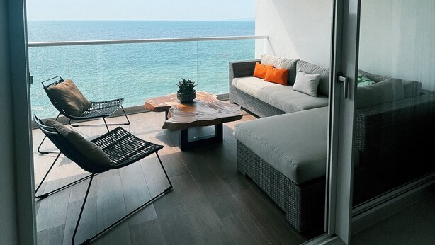 Een balkon met een bank, een stoel en een kleine tafel, met uitzicht op zee.