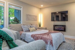 A bedroom with a bed, a sofa, a TV, and a window with a view of trees.