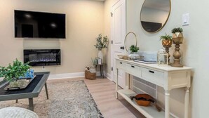 Un salon doté d’un téléviseur à écran plat, d’une cheminée, d’une console blanche et d’un grand miroir.