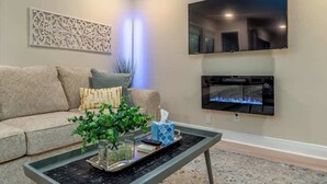 Un salon comprenant un canapé, une table basse avec un vase et une télécommande, un téléviseur à écran plat et une cheminée.