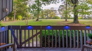 Une terrasse en bois dotée d’une rambarde, d’un espace salon extérieur et offrant une vue sur une zone verdoyante avec des arbres.