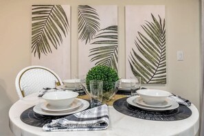A dining table set with white plates, bowls, and a glass. There are three large leaf-patterned wall decorations above the table.