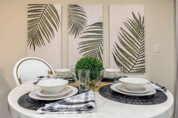 A dining table set with white plates, bowls, and a glass. There are three large leaf-patterned wall decorations above the table.