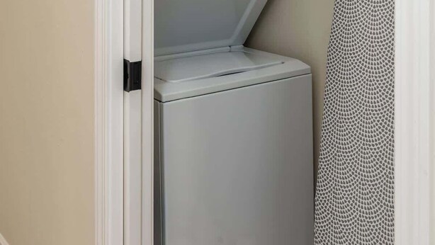 Une petite buanderie équipée d’un lave-linge et d’un sèche-linge, d’un porte-serviettes et d’un certificat encadré accroché au mur.