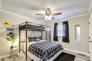 Un dormitorio con literas, ventilador de techo, planta en maceta y cama con colcha a cuadros blanco y negro.