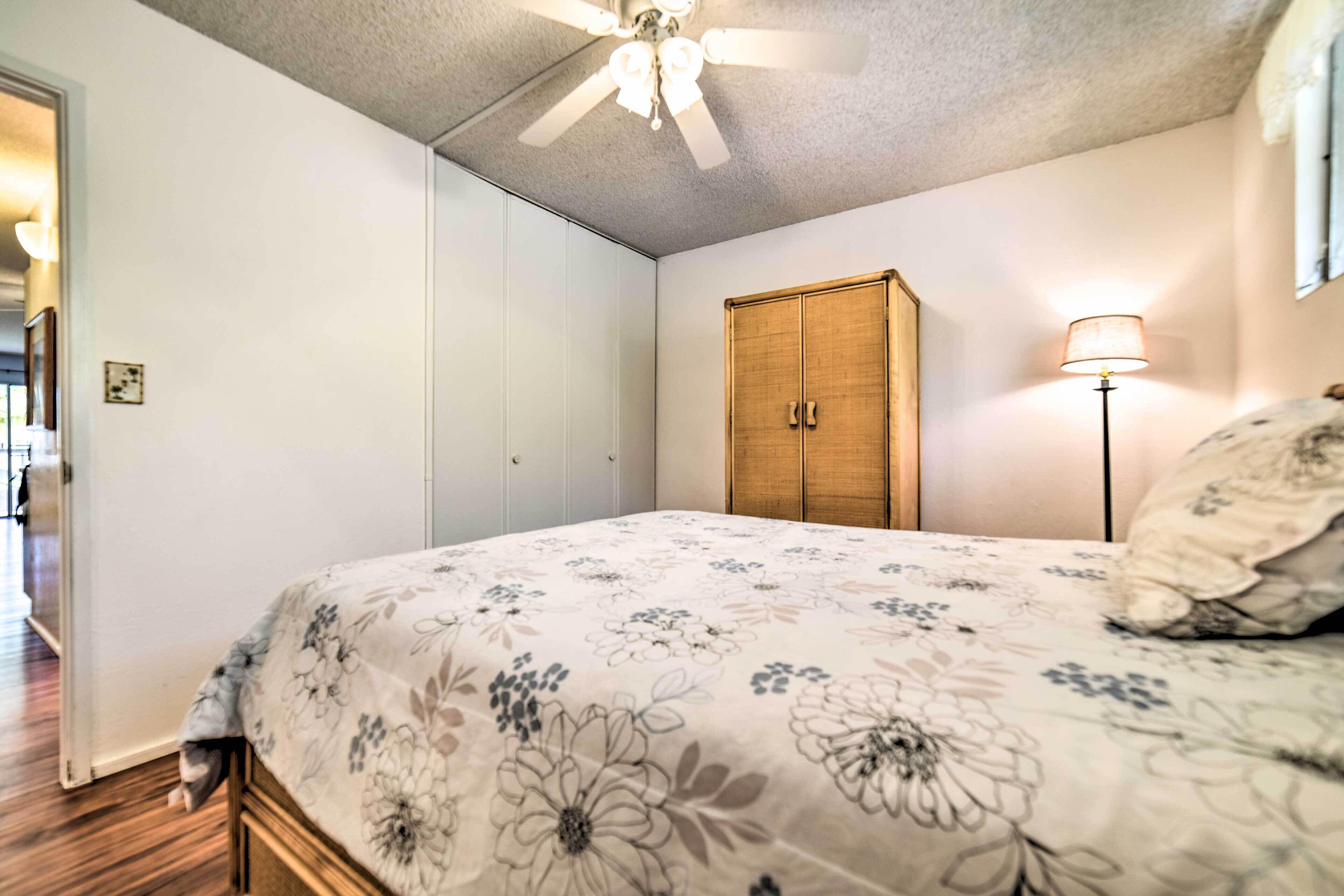 A bedroom with a bed, a ceiling fan, a wardrobe, and a floor lamp.