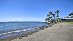 Ein Strand mit einem an das Ufer angrenzenden Gebäude, Palmen und Blick auf den Ozean.