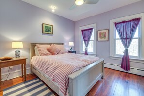 A bedroom with a bed, two bedside tables, a nightstand, a window with curtains, and a ceiling fan.
