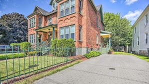 A two-story brick house with a front porch, a paved driveway, and a green fence. - Historic Apartment - Half Mi to Lake Champlain! (Plattsburgh)
