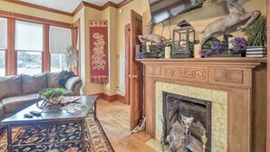A living room with a fireplace, a sofa, a coffee table, and a television mounted on the wall. - Historic Apartment - Half Mi to Lake Champlain! (Plattsburgh)