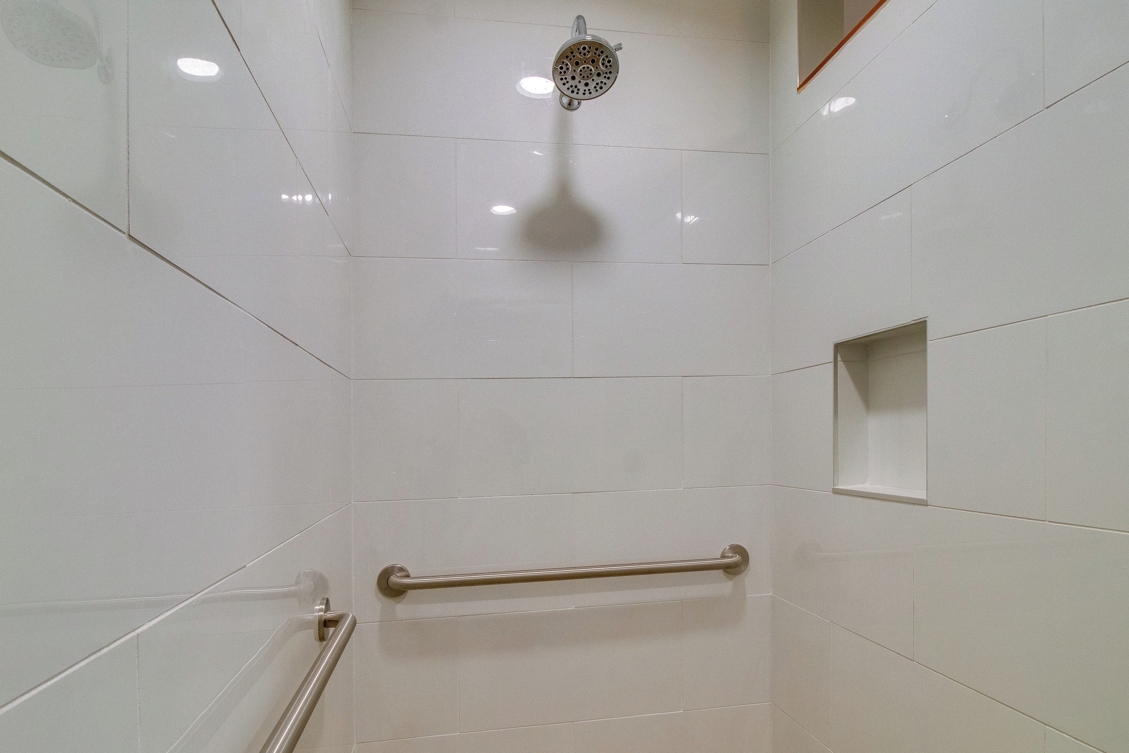 Een douche met een handdouche, een handgreep en een klein plankje.
