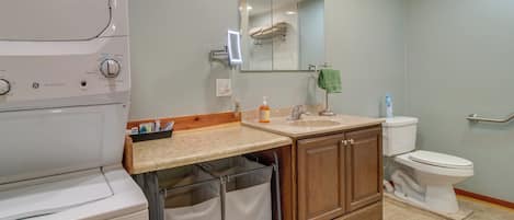 A modern bathroom with a built-in washer, a vanity with a mirror, a toilet, and a trash can.