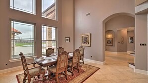 A dining room with a large table and chairs, large windows, and a view of the outside.