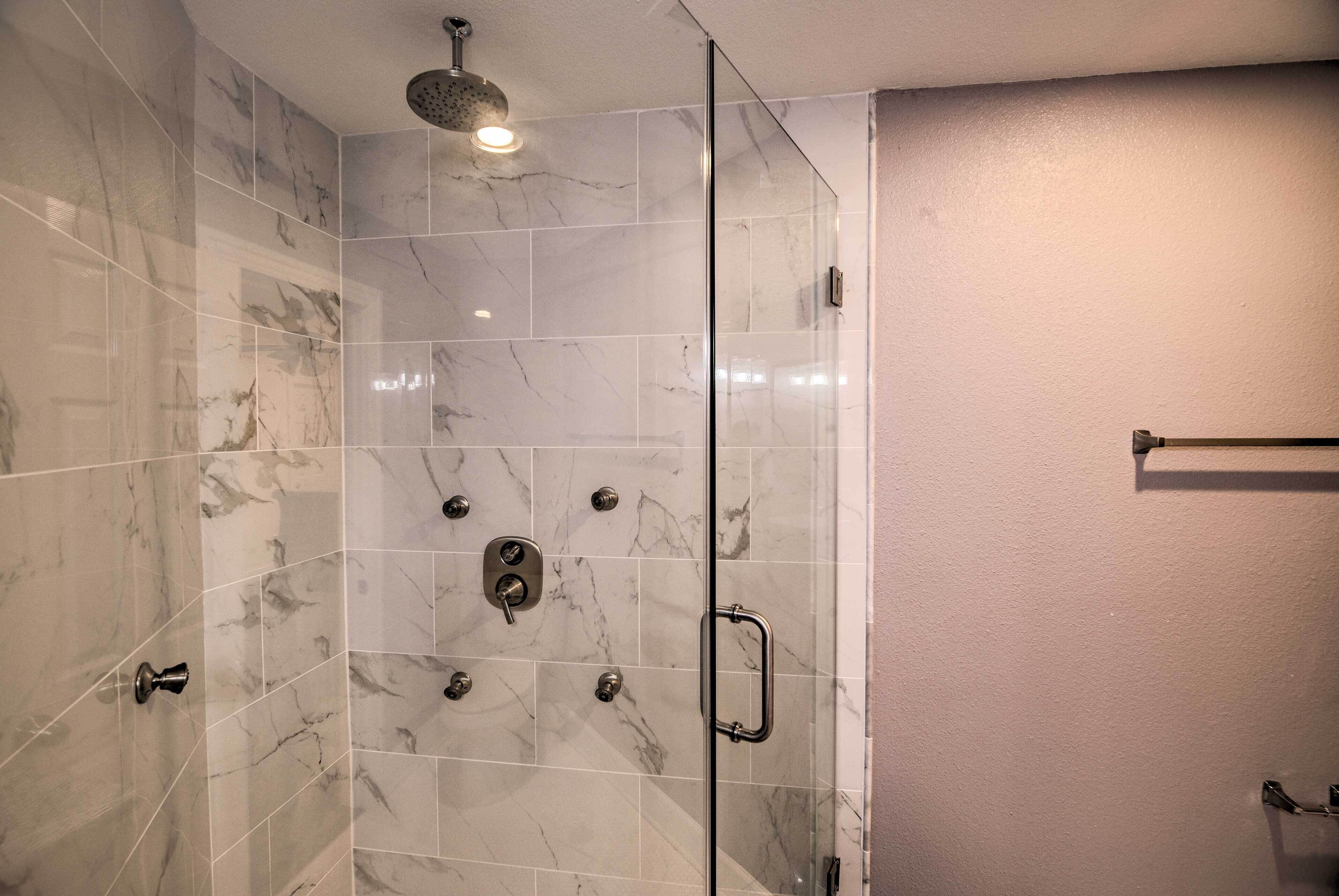A shower with a glass door, marble tiles, and a handheld showerhead.