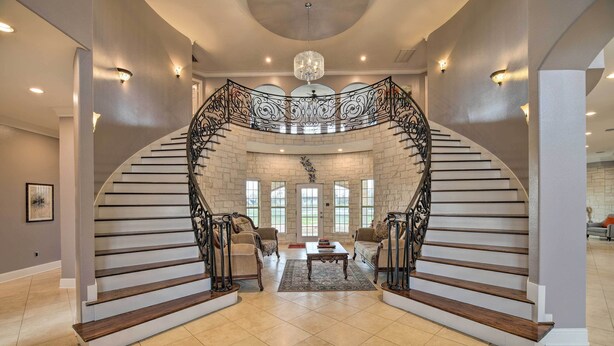 A grand staircase with a wrought iron railing leading to a landing area with two sofas and a coffee table.