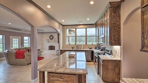 A spacious kitchen with a large island, wooden cabinets, and a stone fireplace.
