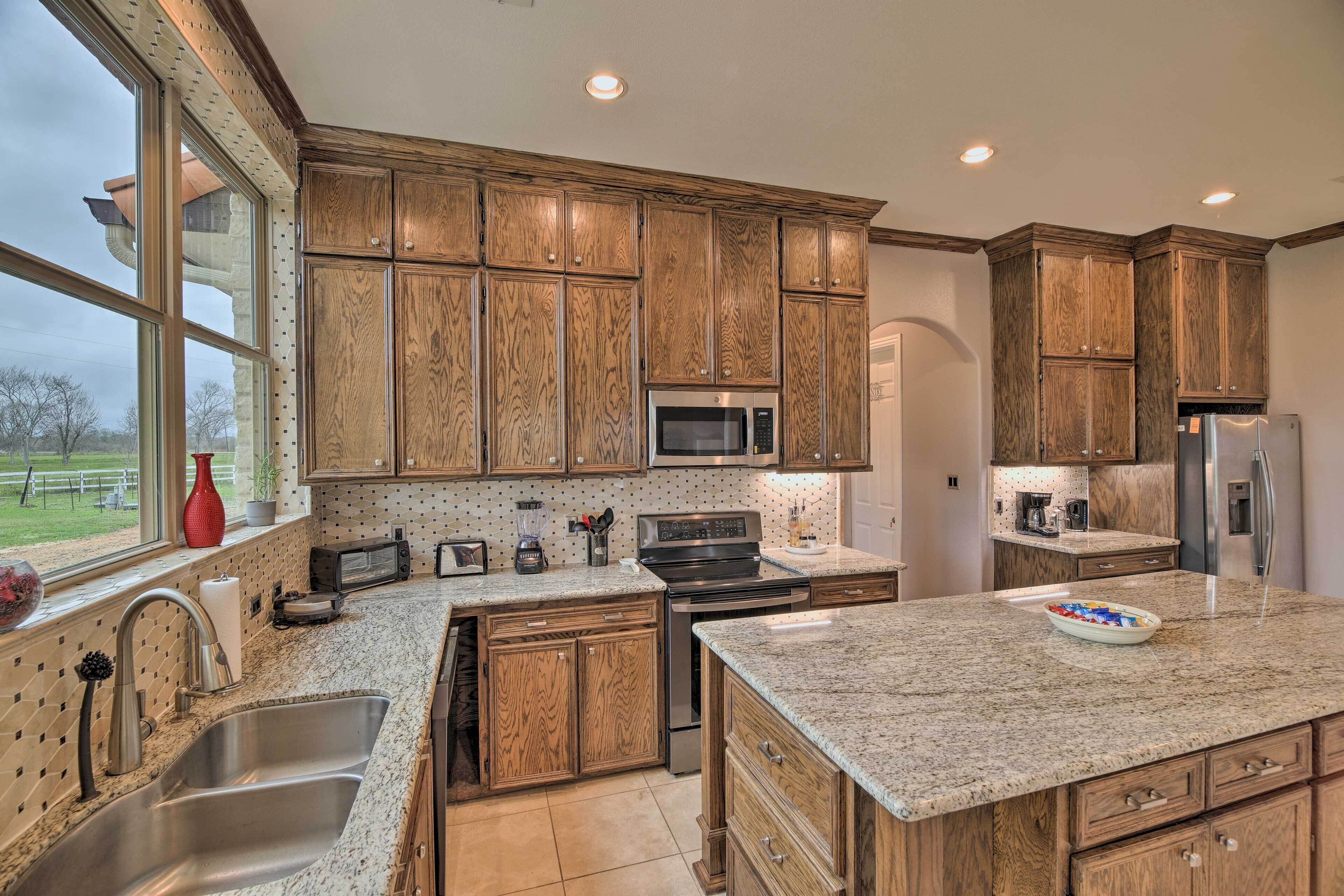A kitchen with wooden cabinets, stainless steel appliances, granite countertops, and a large window offering a view of the outdoors.