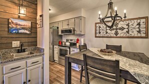 A kitchen with granite countertops, white cabinets, a stainless steel sink, and a wooden backsplash. There is a dining table with chairs and a chandelier above it. - Deck & Grill: Modern Sugar Mtn Escape! (Banner Elk)