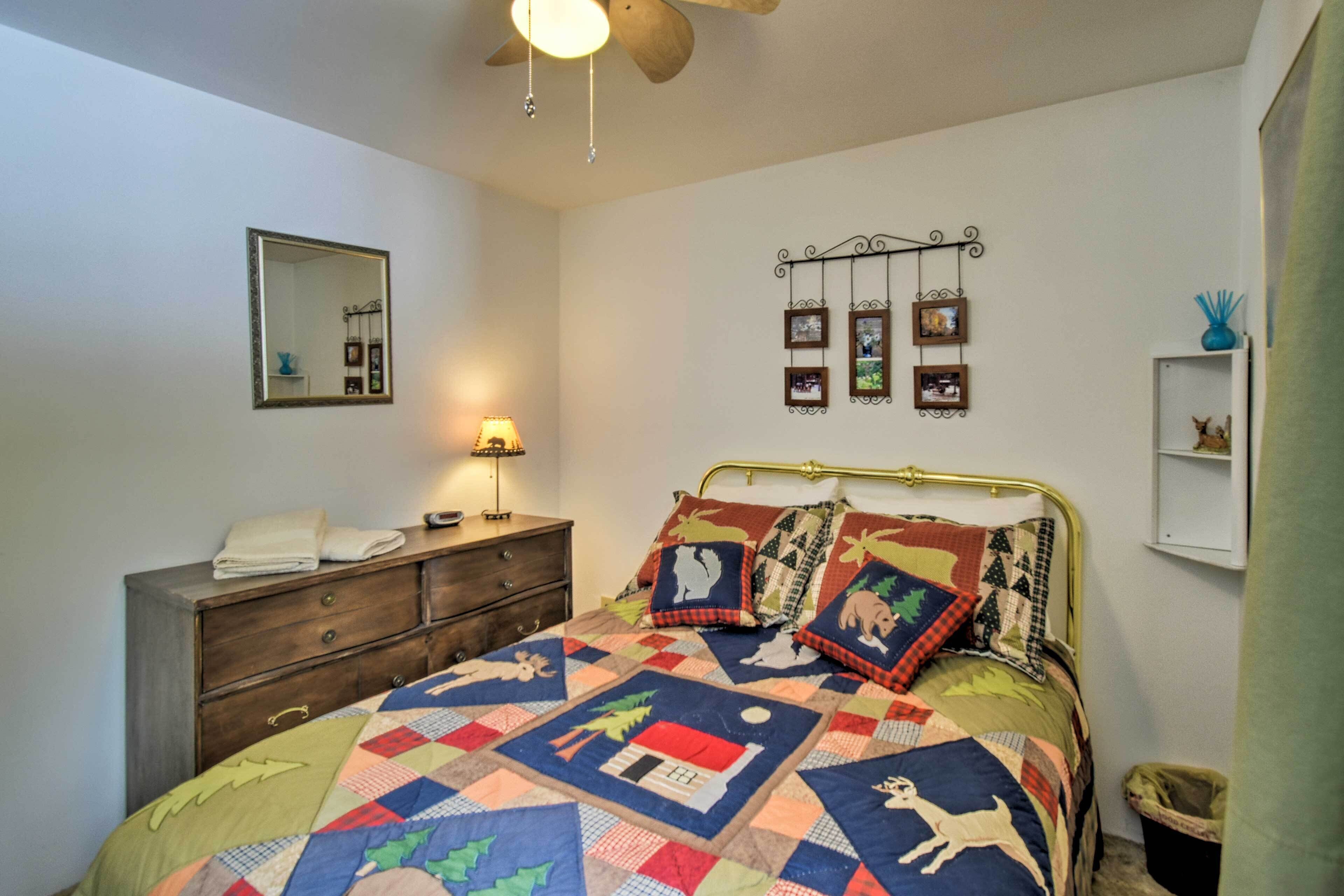 A bedroom with a bed, dresser, mirror, wall-mounted pictures, and a ceiling fan.