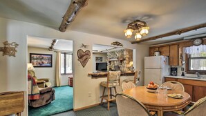 Una sala de estar acogedora con chimenea, un comedor con mesa y sillas de madera, y una cocina con armarios de madera y un refrigerador.