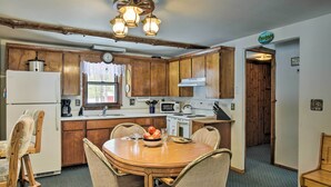 Una cocina con armarios de madera, un refrigerador blanco, un microondas y una mesa de comedor con sillas.