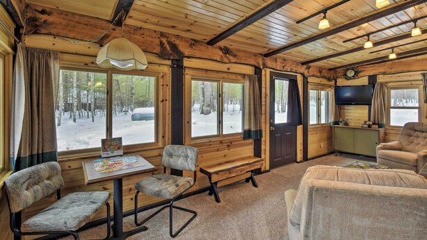 Un interior de cabaña acogedor, con techo de madera, ventanas amplias, televisión y chimenea.