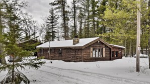 Una cabaña de troncos con techo nevado, rodeada de altos pinos.