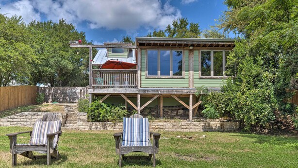 Eine Holzterrasse mit zwei Adirondack-Stühlen, eine kleine, erhöhte Struktur mit einem Fenster und eine Steinmauer im Hintergrund.
