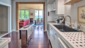 Eine Küche mit einem schwarzen Spülbecken, weißen Schränken und einer Holzausziehtafel. Durch einen offenen Durchgang ist ein Essbereich mit Tisch und Stühlen zu sehen.