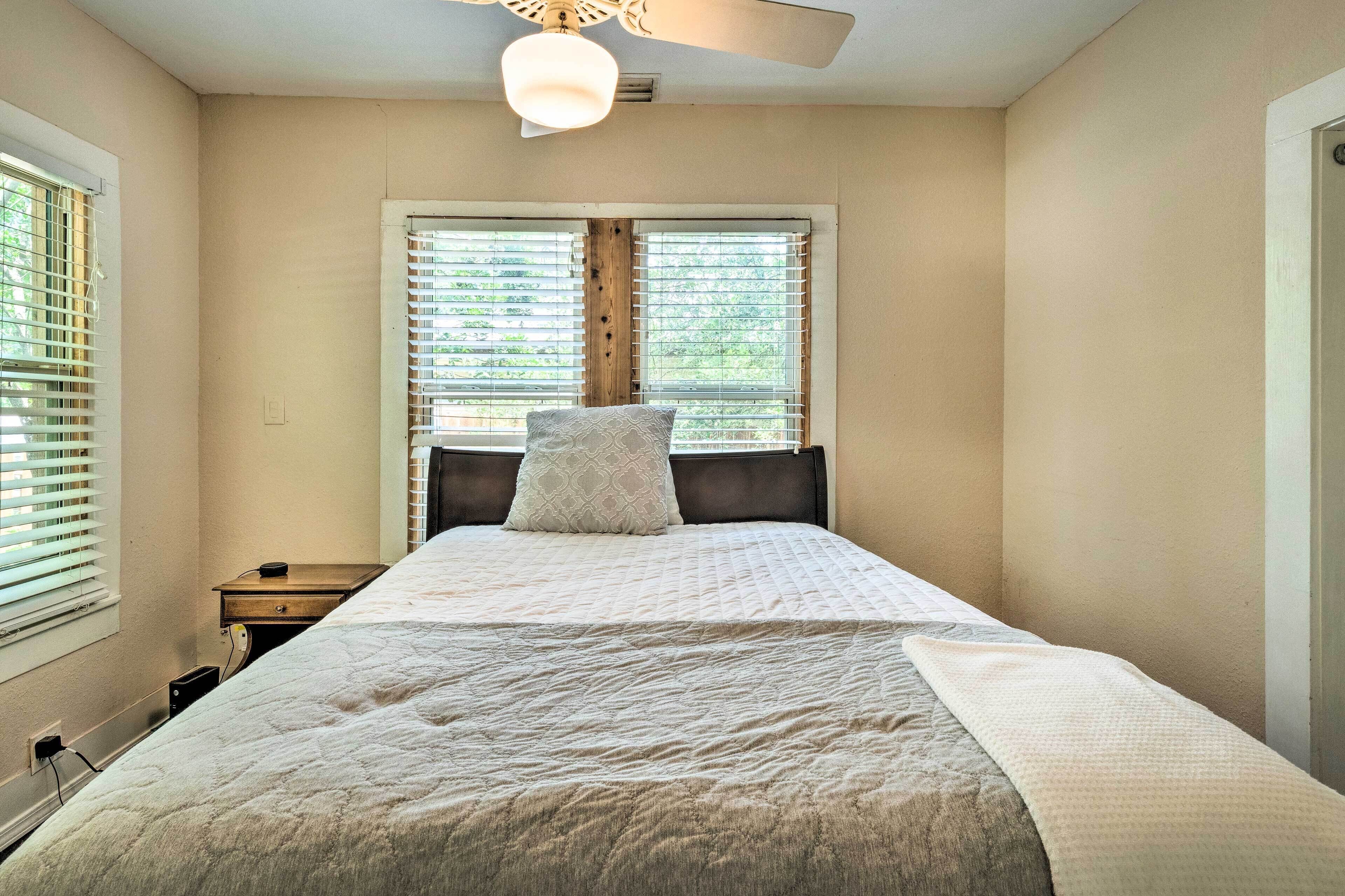 A bedroom with a bed, a nightstand, a ceiling fan, and a window with blinds.