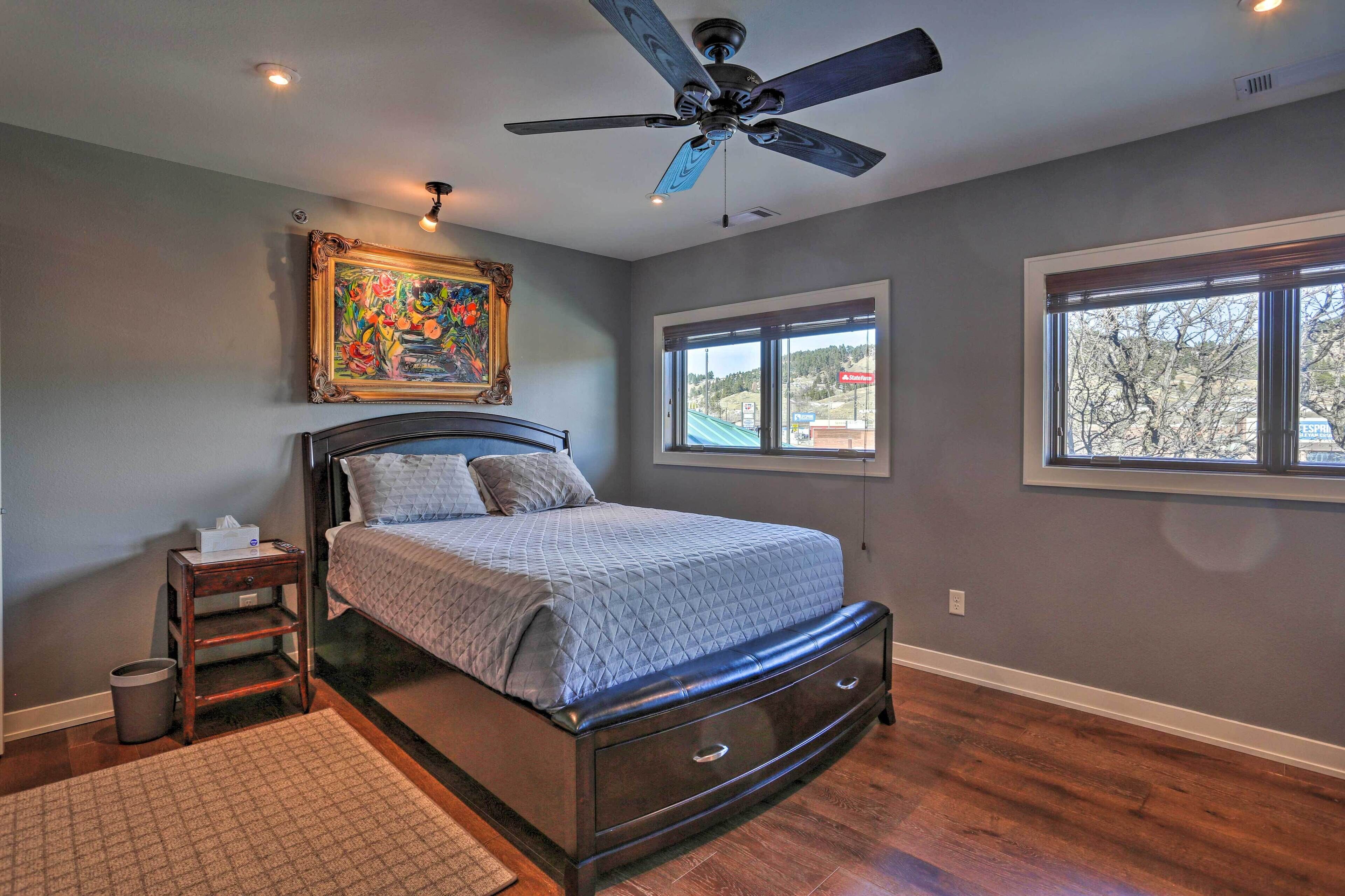 A bedroom with a bed, a ceiling fan, a window, and a painting on the wall.