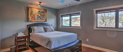 A bedroom with a bed, a ceiling fan, a window, and a painting on the wall.