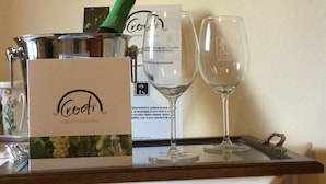 A wine bottle, two wine glasses, and a card on a tray. - Sleeping in the Prosecco Hills. House suitable for families or groups of friends. (Combai)